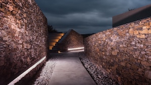 A stone-walled corridor with a concrete path leading to a triangular structure.