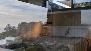 A bedroom with a large window, a bed with patterned bedding, a bedside table with a lamp, and a view of the outdoors.