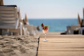 A wooden deck with a drink on a glass, beach chairs, and the ocean in the background. - Elysee Beach Hotel (Alanya)