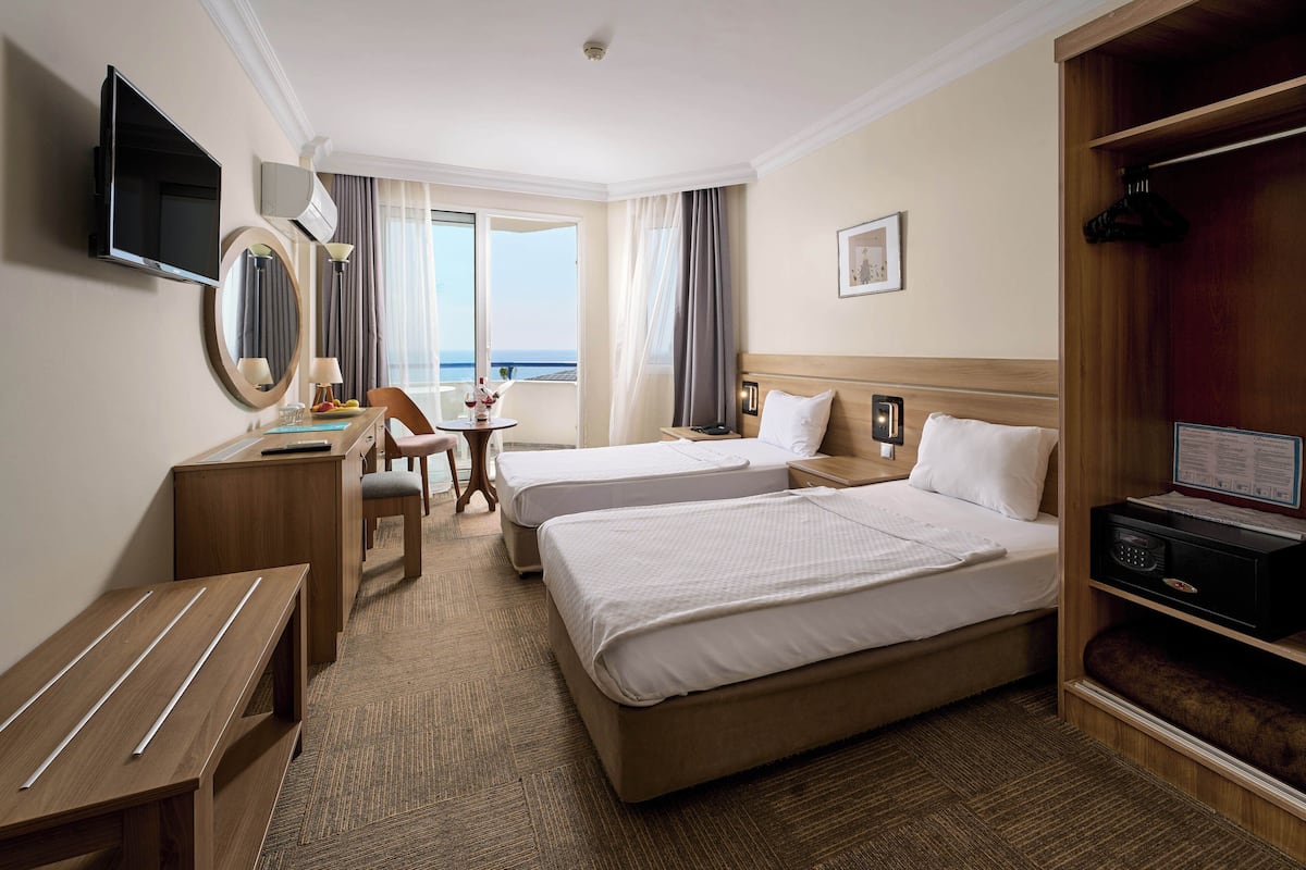 Ein Hotelzimmer mit zwei Betten, einem Schreibtisch, einem Sessel, einem Fernseher, einem Spiegel und Meerblick.