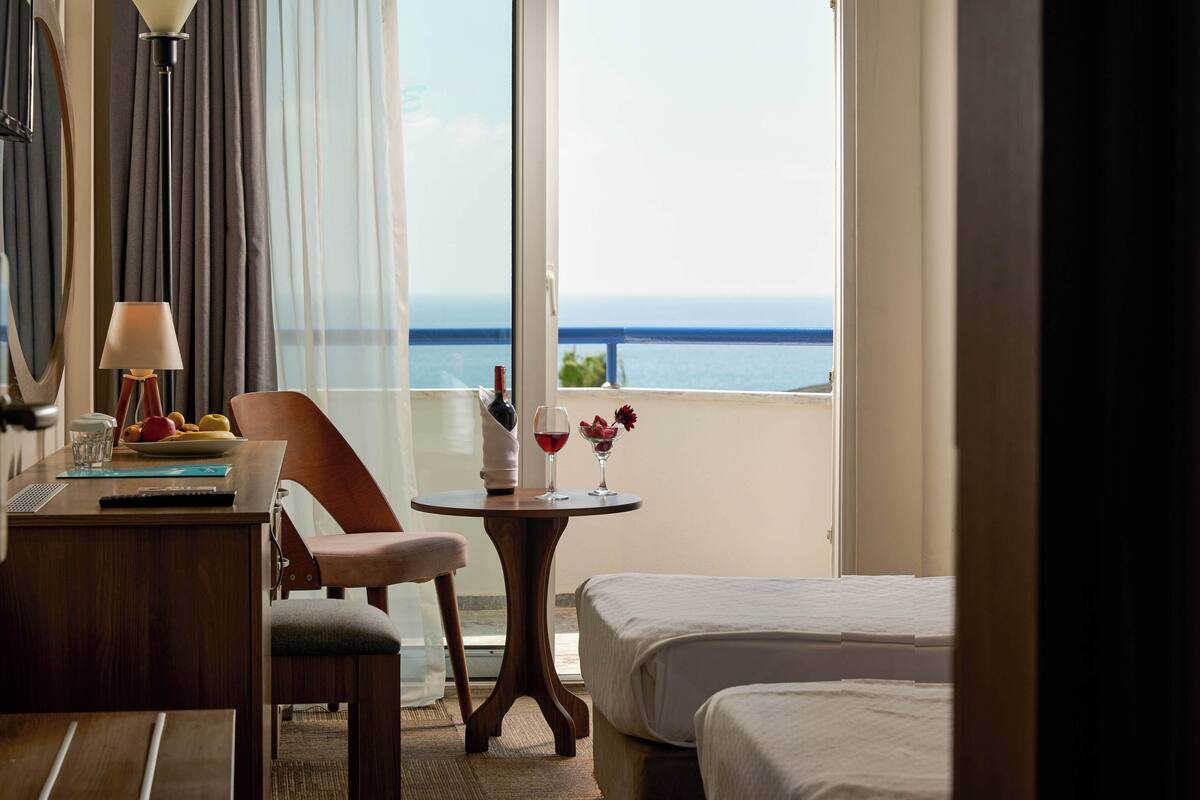 Ein Hotelzimmer mit Bett, einem kleinen Tisch mit Lampe, einem Sessel und Blick auf den Ozean.