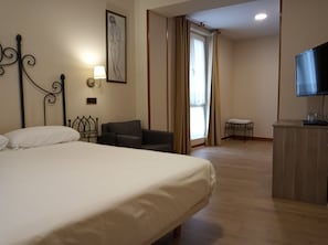 A hotel room with a large bed, a desk, a chair, a television, and a window with curtains. - Pensión Begoña (Bilbao)
