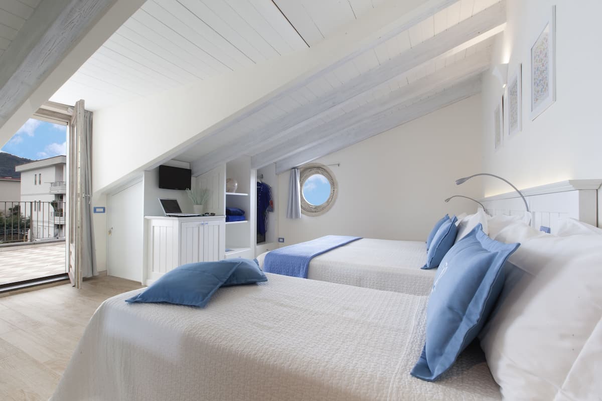 Ein Schlafzimmer mit zwei Betten, einem Laptop auf einem Schreibtisch und Blick ins Freie.