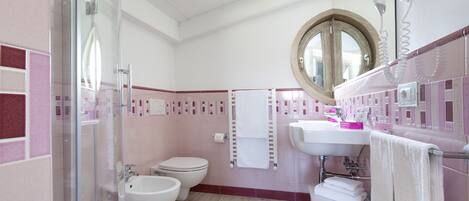 Et badeværelse med brusekabine i glas, toilet, bidet og vask med spejl over.