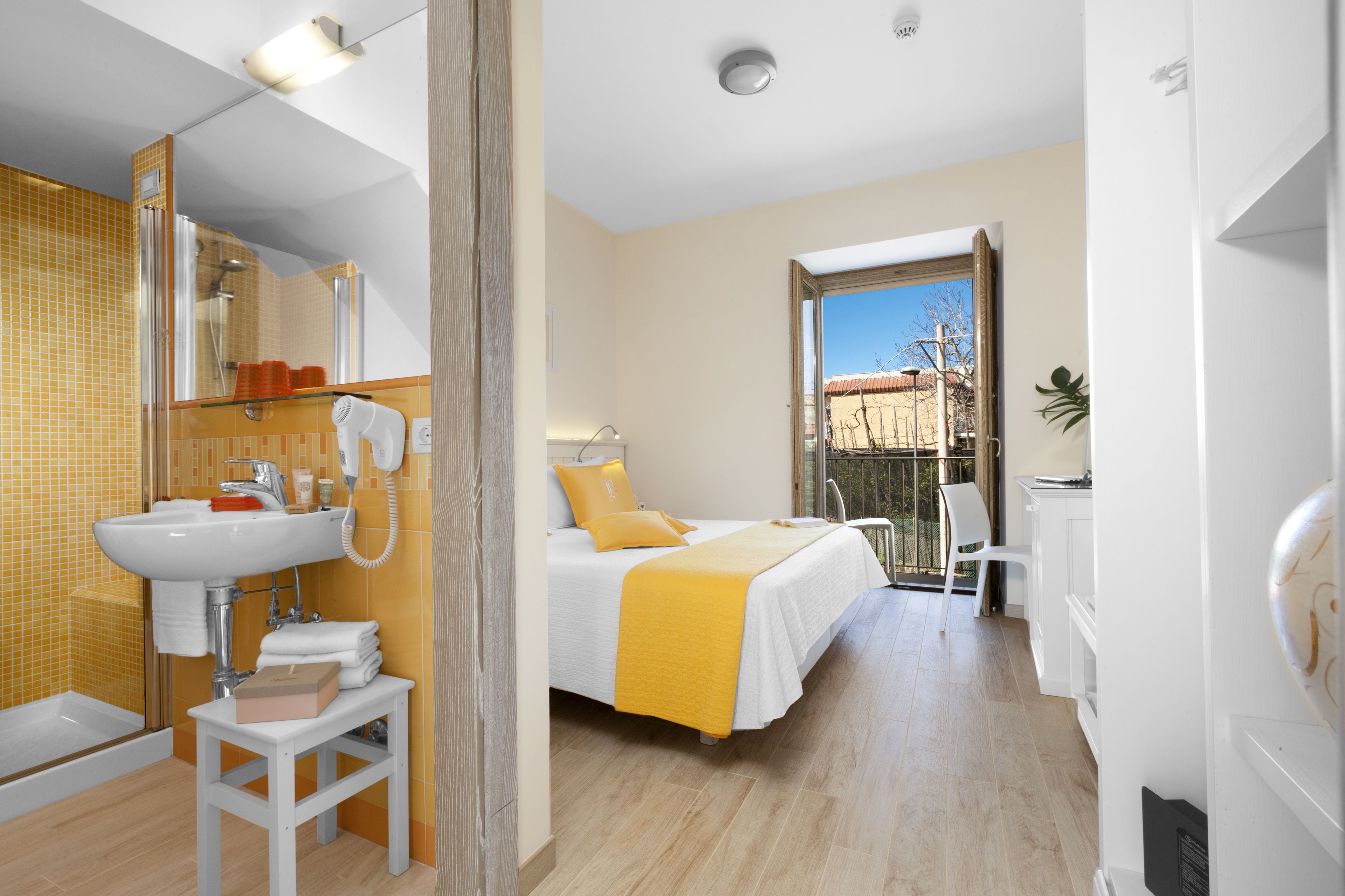 A hotel room with a bed, a bathroom with a sink and mirror, and a view of the outside.