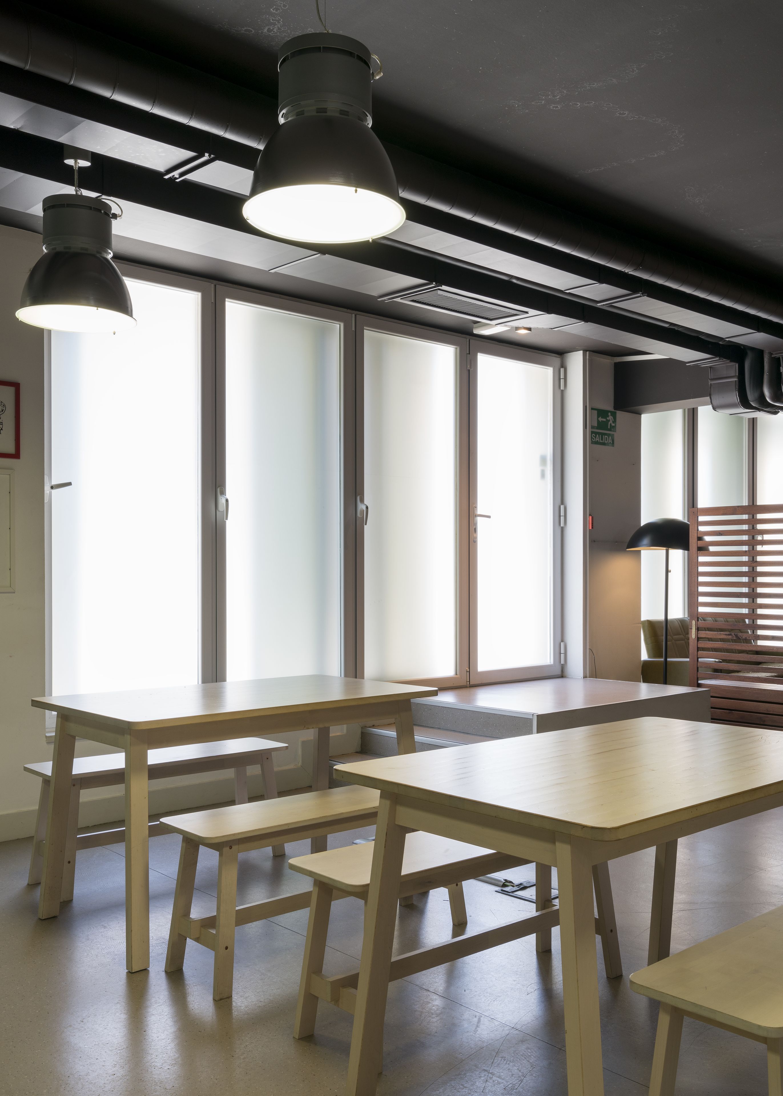 Un interior moderno con amplios ventanales, varias mesas e iluminación colgante.