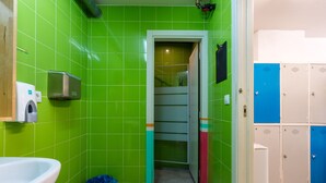 A bathroom with green tiles, a white sink, a trash bin, and a set of lockers. - Hostal Ganbara (Bilbao)