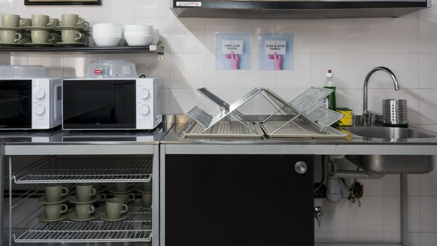 A kitchen with stainless steel appliances, a sink, and shelves with plates and cups. - Hostal Ganbara (Bilbao)