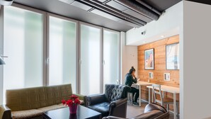 A modern interior with a sofa, a table with a vase, and a person working at a desk. - Hostal Ganbara (Bilbao)