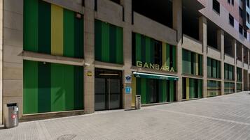 Un edificio con fachada verde y amarilla, un letrero que dice 'GANBARA HOSTEL' y una entrada accesible para sillas de ruedas.