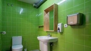 A bathroom with green tiles, a white sink, a wooden cabinet, and a toilet. - Hostal Ganbara (Bilbao)