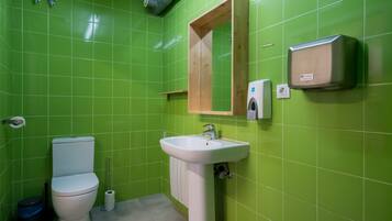 Un baño con azulejos verdes, un lavamanos blanco, un armario de madera y un inodoro.