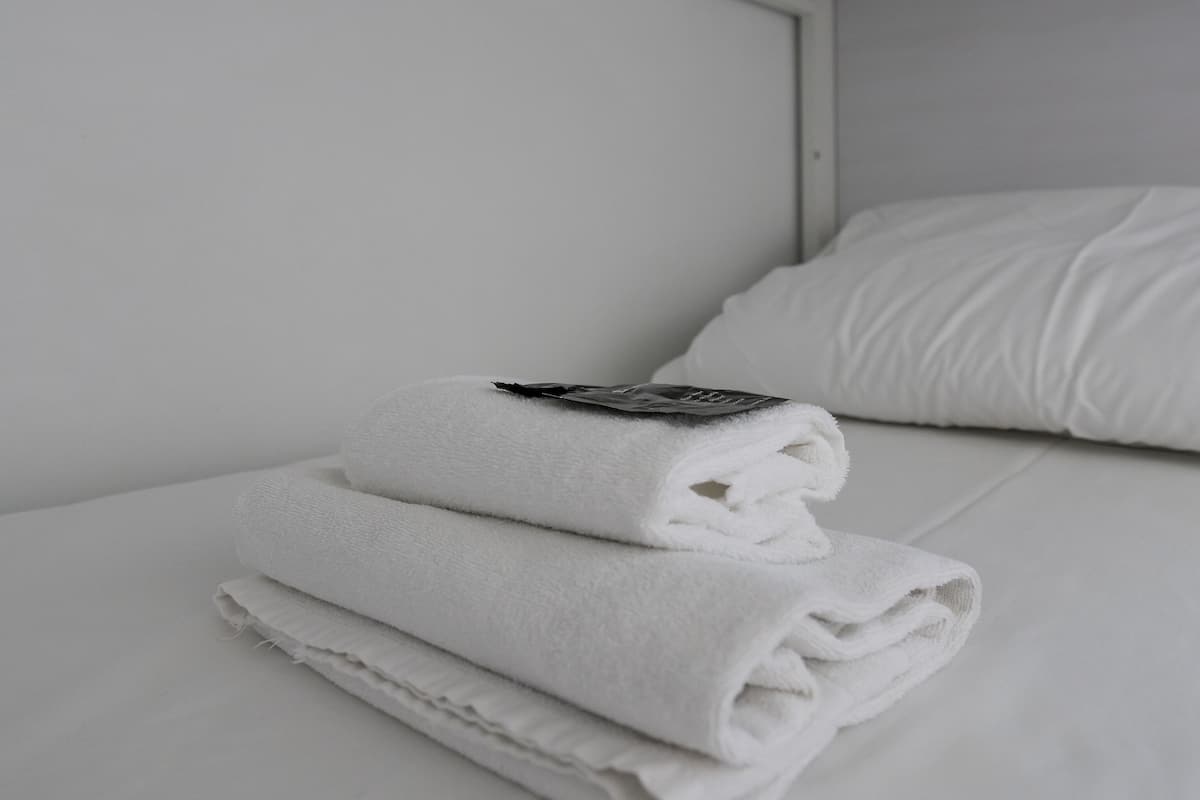 Una cama bien hecha con sábanas blancas y una toalla doblada encima.