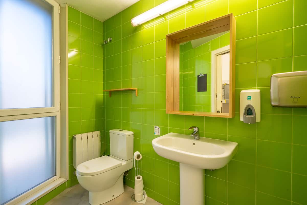 Un baño con azulejos verdes, inodoro blanco, lavamanos y espejo.