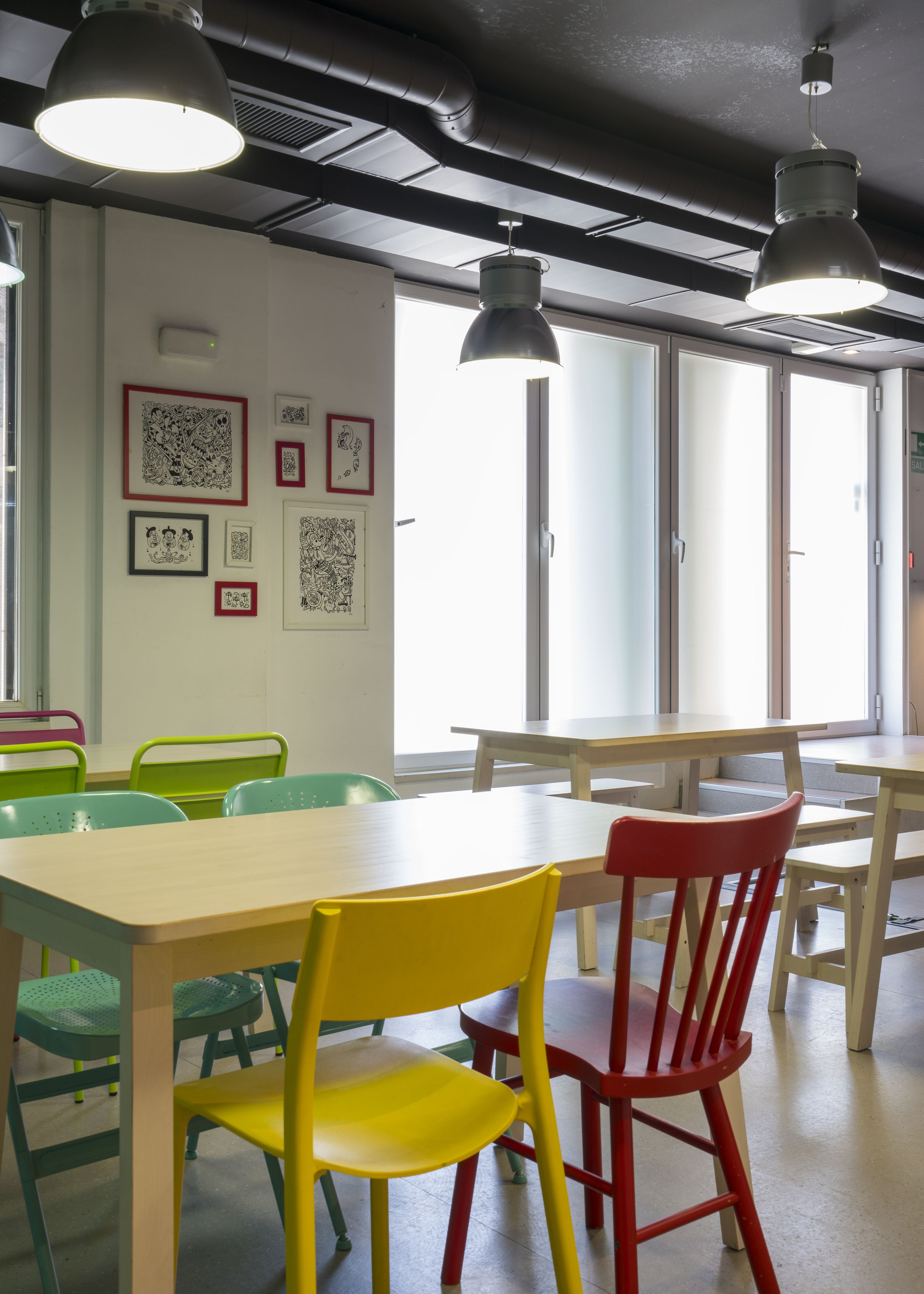A room with tables and chairs, artwork on the wall, and large windows.