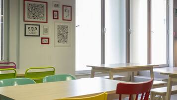 A room with tables and chairs, artwork on the wall, and large windows.
