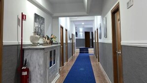 A hotel hallway with a blue carpet, wooden doors, and a fire extinguisher on the left. - Hotel Martini (Casavatore)