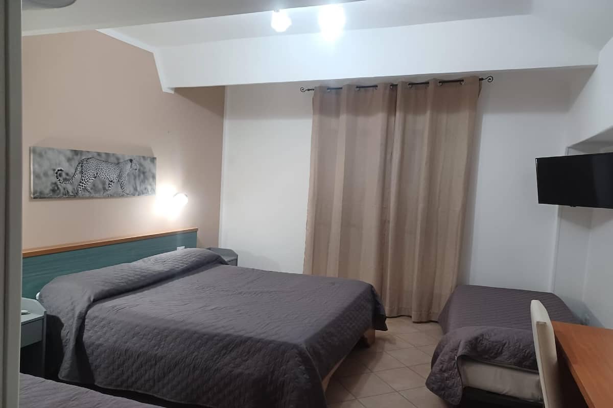 A hotel room with two beds, a flat-screen TV, a painting on the wall, and a window with curtains.