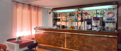 A bar area with a counter, shelves of beverages, a coffee machine, and a seating area with chairs and a table.