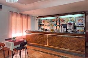 A bar area with a counter, shelves of beverages, a coffee machine, and a seating area with chairs and a table. - Hotel Martini (Casavatore)