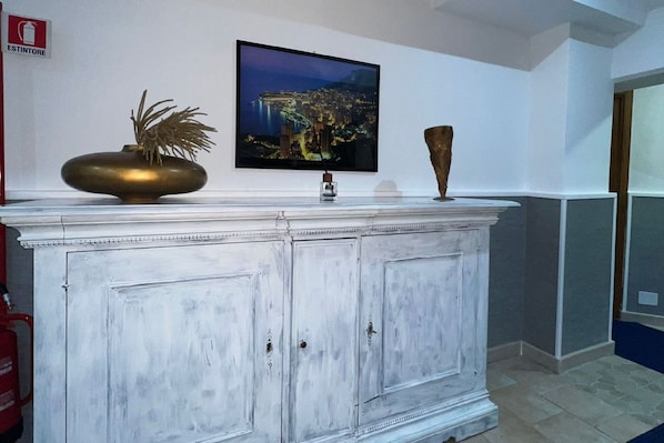 A white cabinet with a television mounted above it, a decorative vase, and a fire extinguisher on the wall. - Hotel Martini (Casavatore)