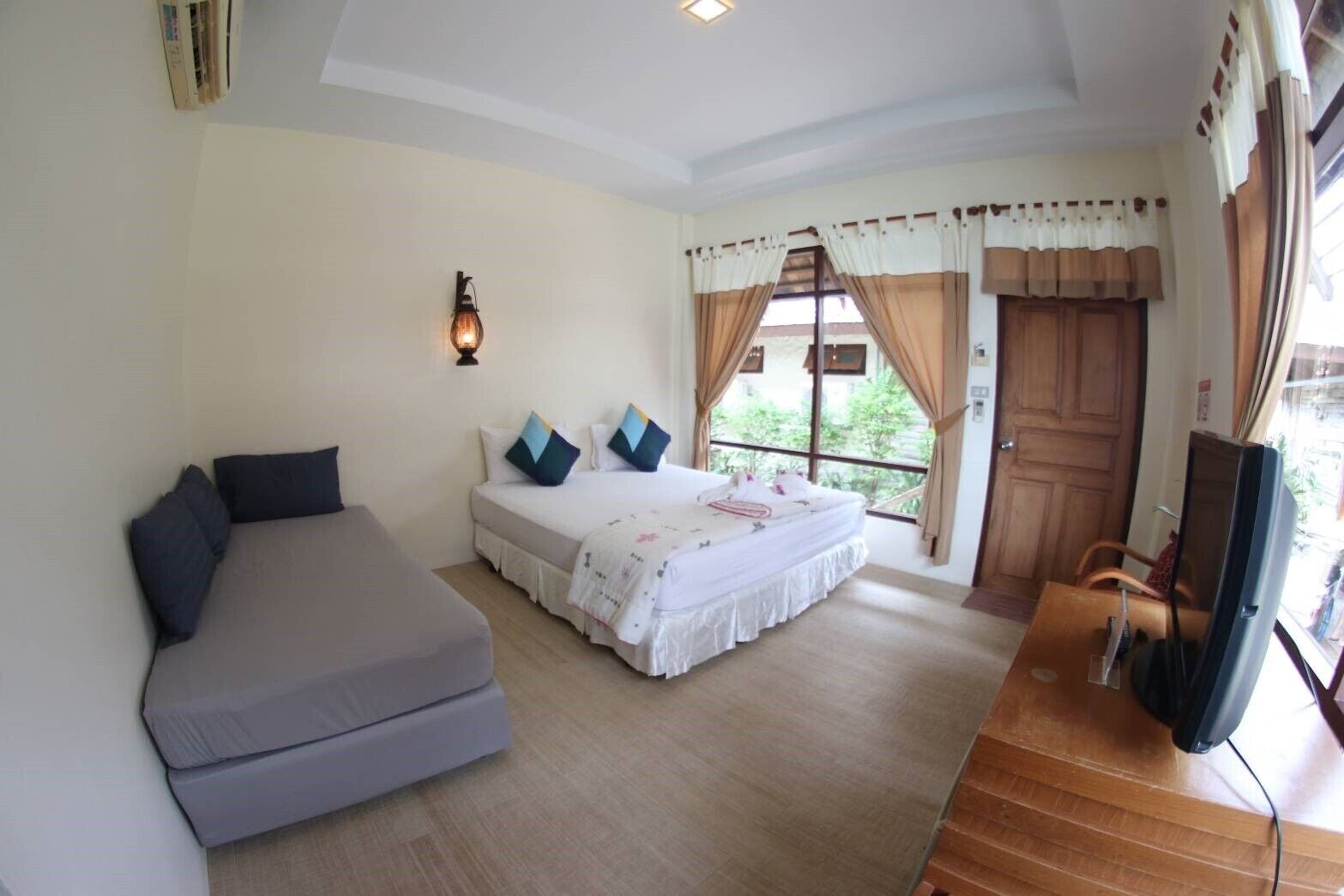 A bedroom with a bed, a sofa, a TV, and a window with curtains.