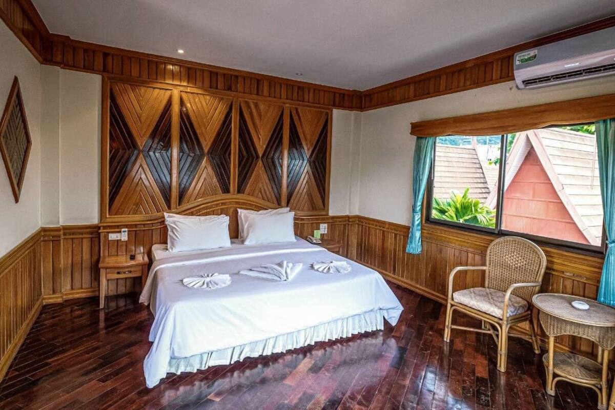 A hotel room with a wooden paneled headboard, a bed with white linens, a wicker chair, and a window with curtains.
