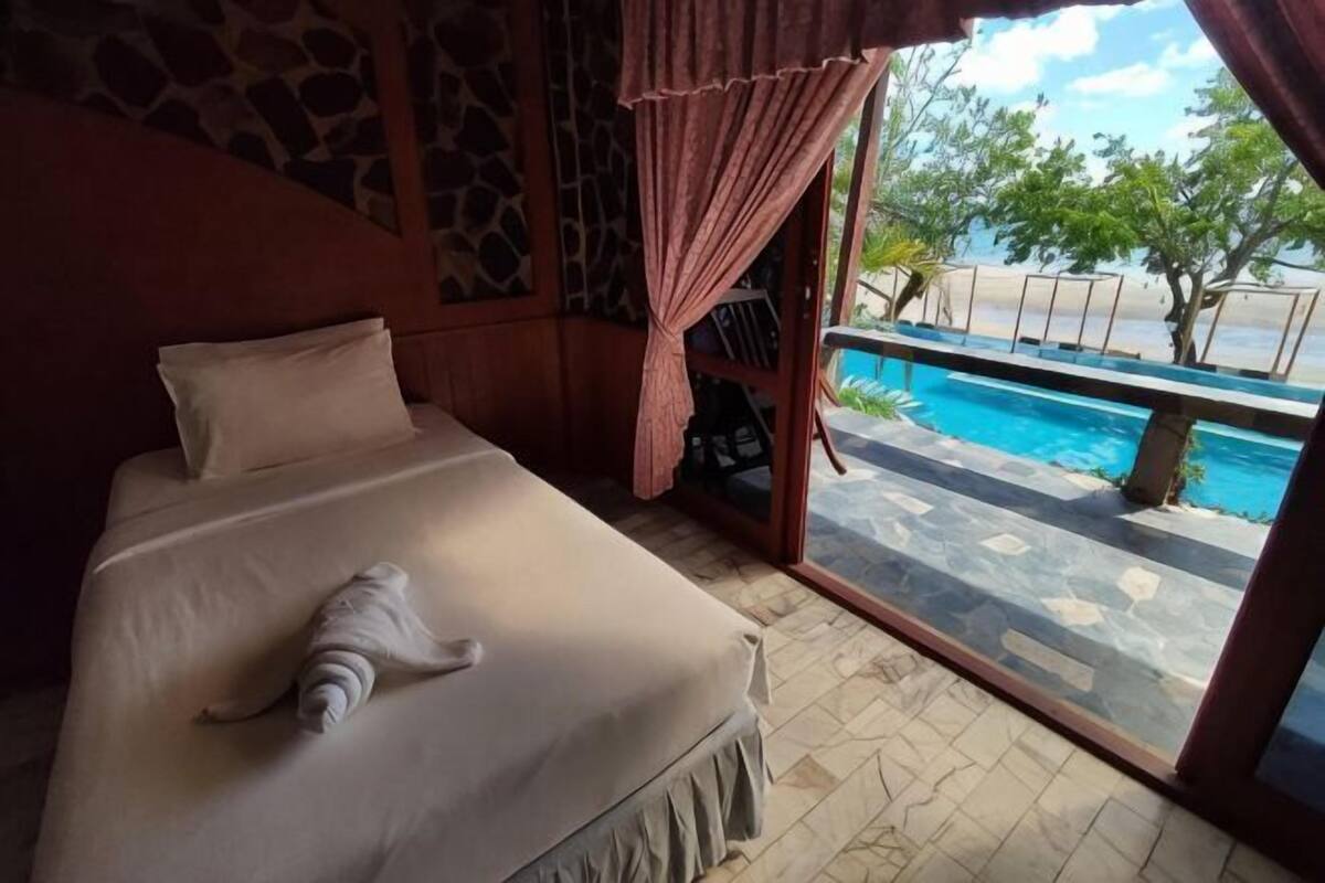 A room with a bed, a view of a swimming pool, and a stone wall.