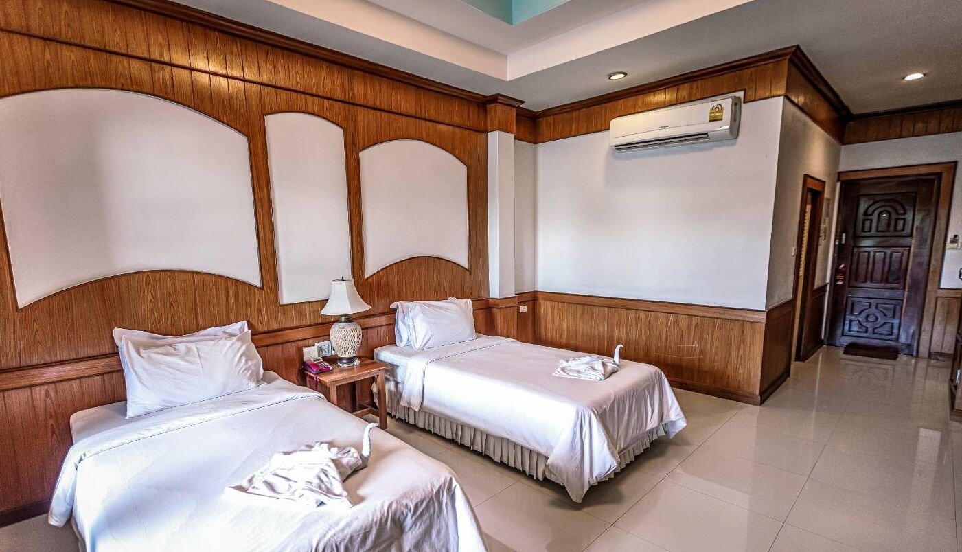 A hotel room with two beds, wooden paneling, a nightstand with a lamp, and an air conditioning unit on the wall.