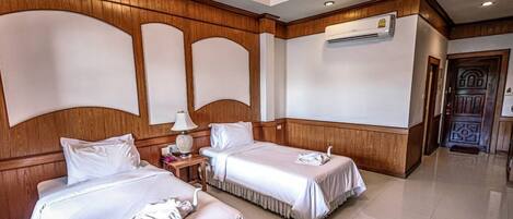 A hotel room with two beds, wooden paneling, a nightstand with a lamp, and an air conditioning unit on the wall.
