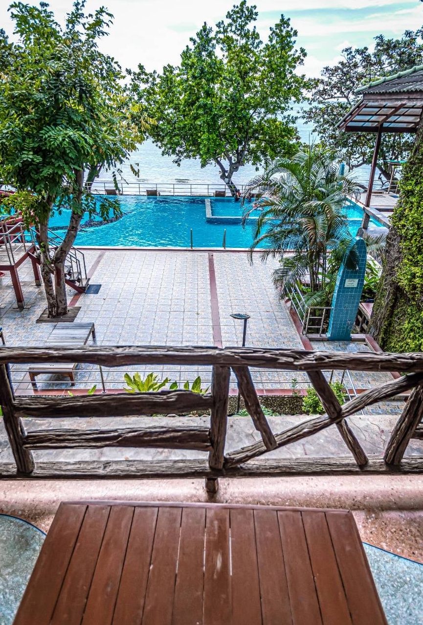 A pool area with a wooden deck, a view of the sea, and a covered seating area.