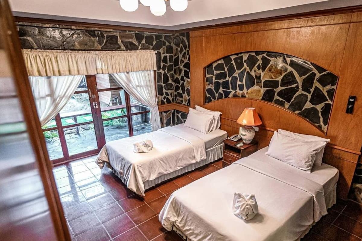 A hotel room with two beds, a stone accent wall, a wooden headboard, and a view through a large window.