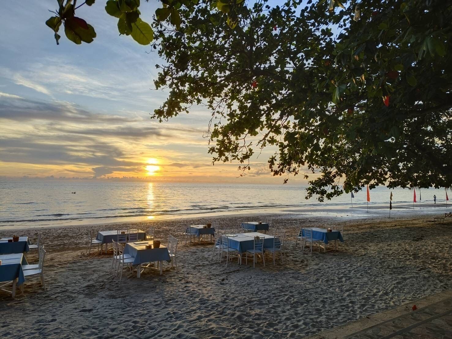 Un restaurante frente al mar con mesas y sillas dispuestas sobre la arena, con vista al océano.