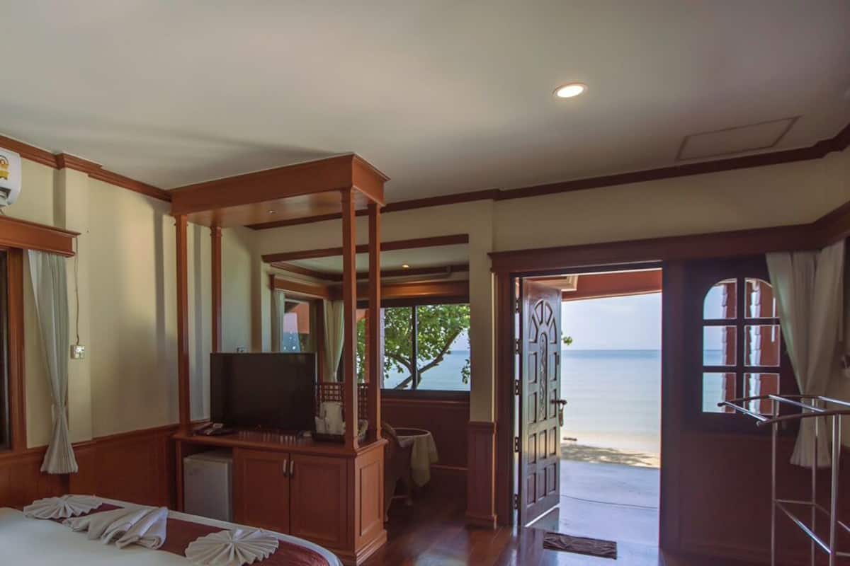A hotel room with a bed, a desk, a television, and a view of the beach.