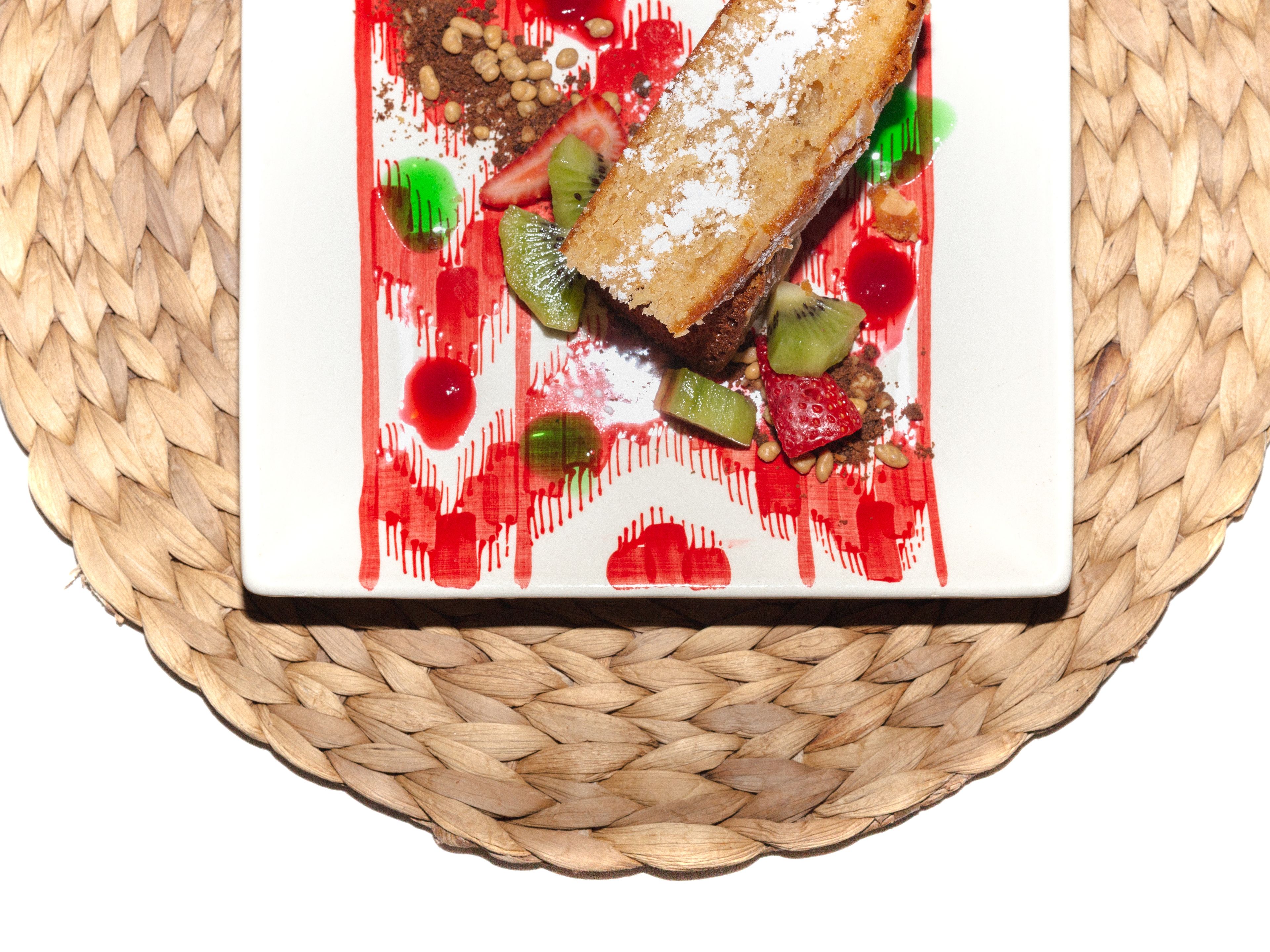 A square plate with a dessert on a woven mat.