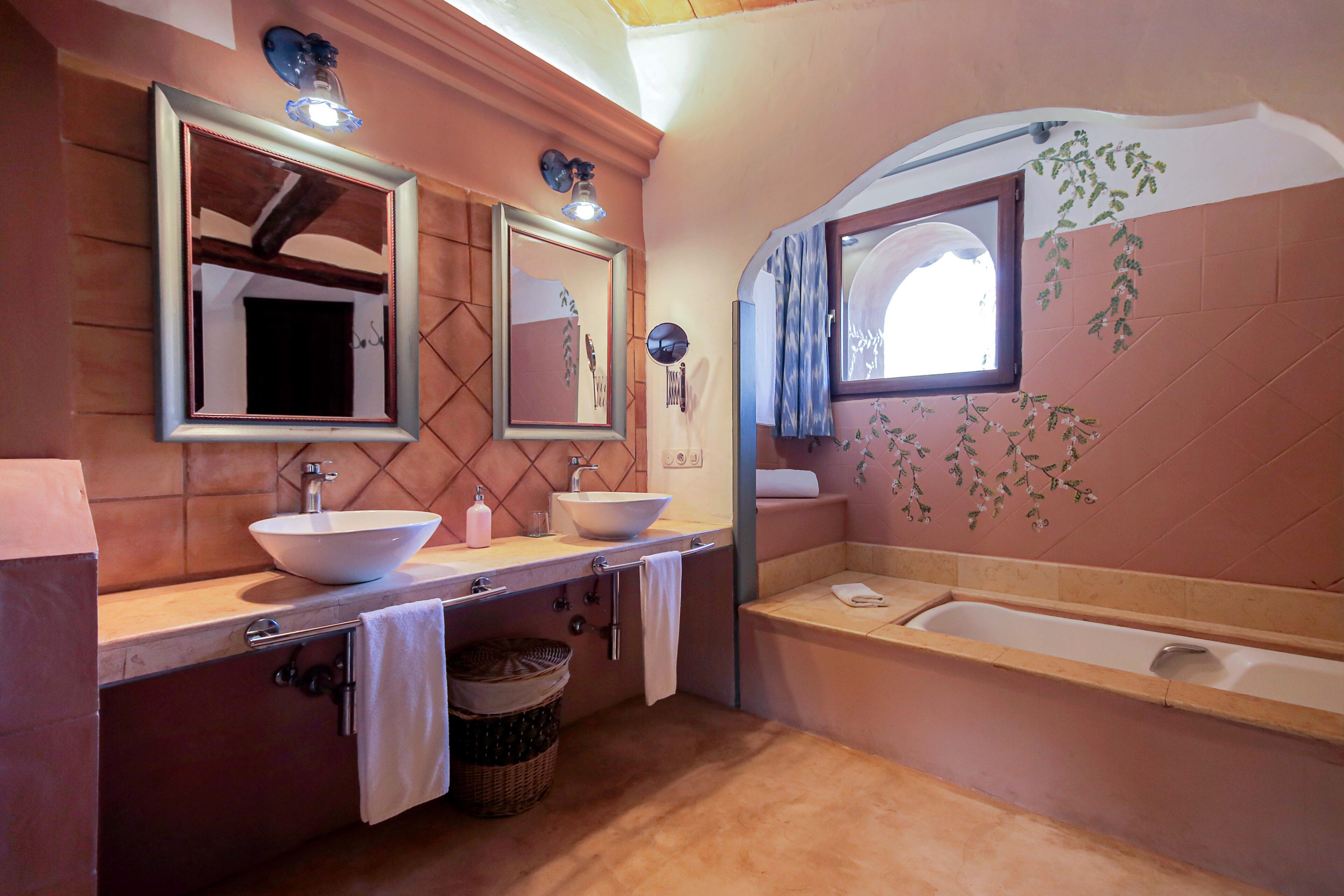 Une salle de bain avec un grand lavabo, deux miroirs, une baignoire et une fenêtre donnant sur l’extérieur.