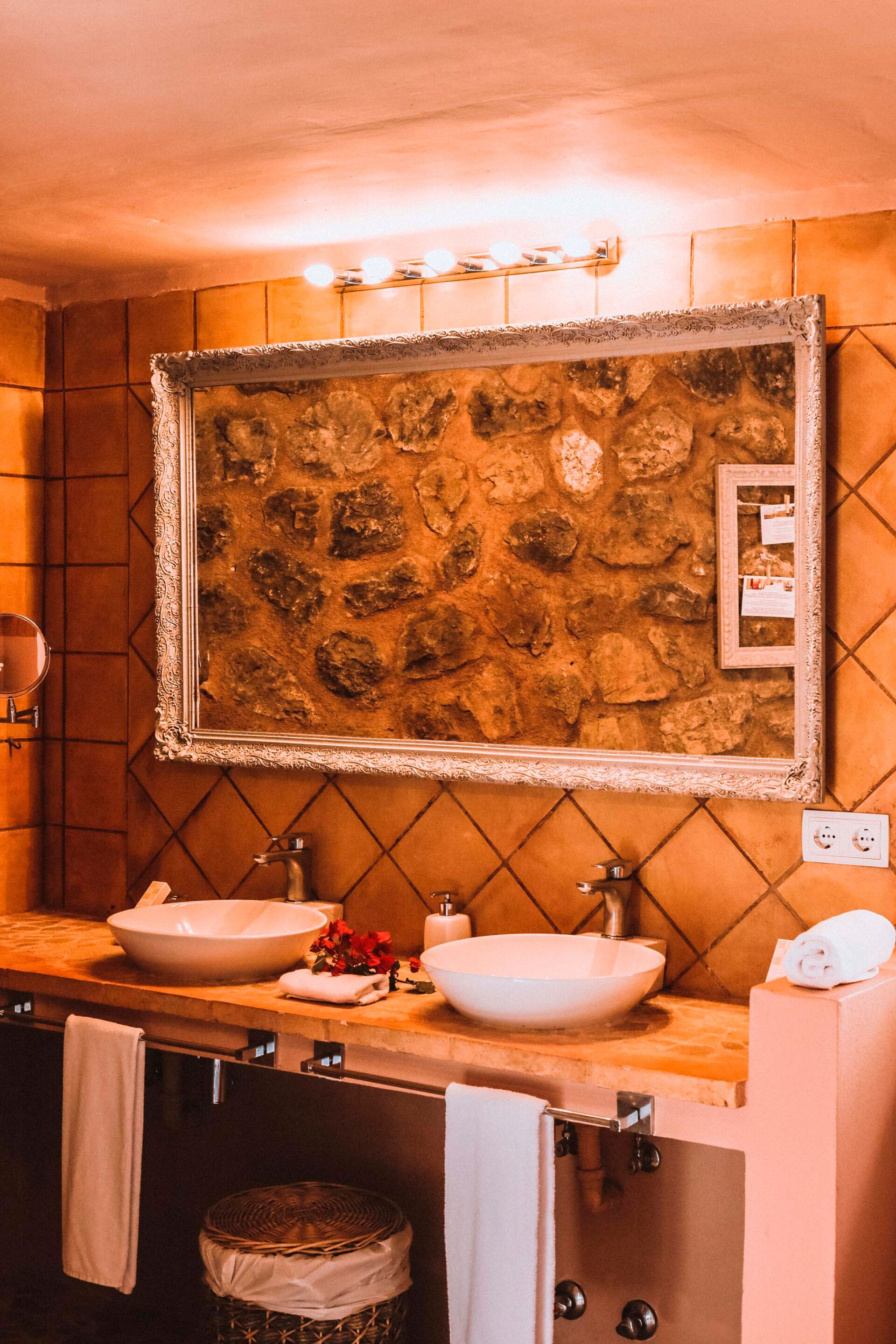 A bathroom with two sinks, a stone wall, and a framed mirror.