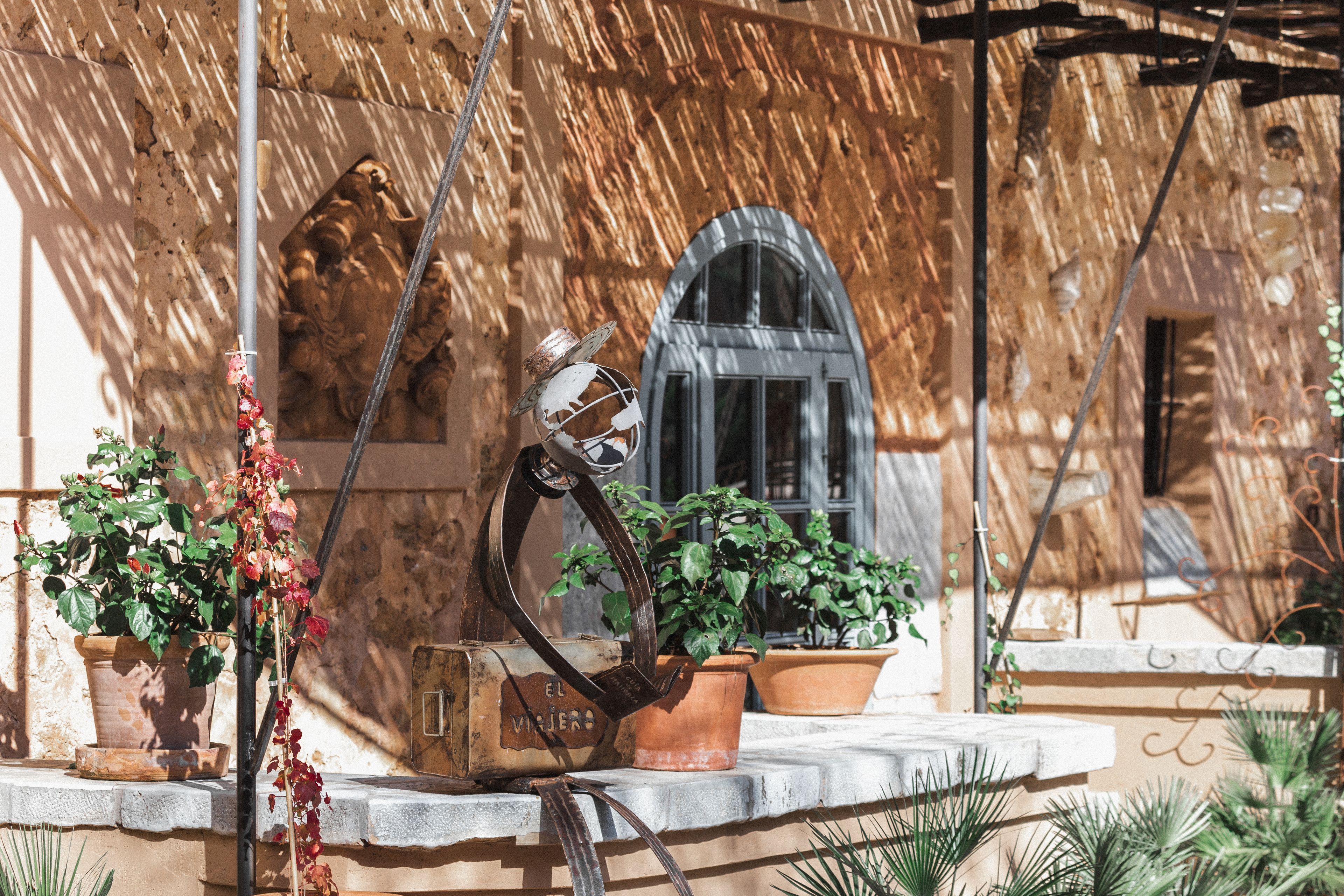A rustic outdoor setting with a stone wall, a metal sculpture, and potted plants.
