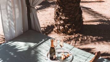 A hammock under a canopy, a table with a bottle and glasses, and a palm tree.