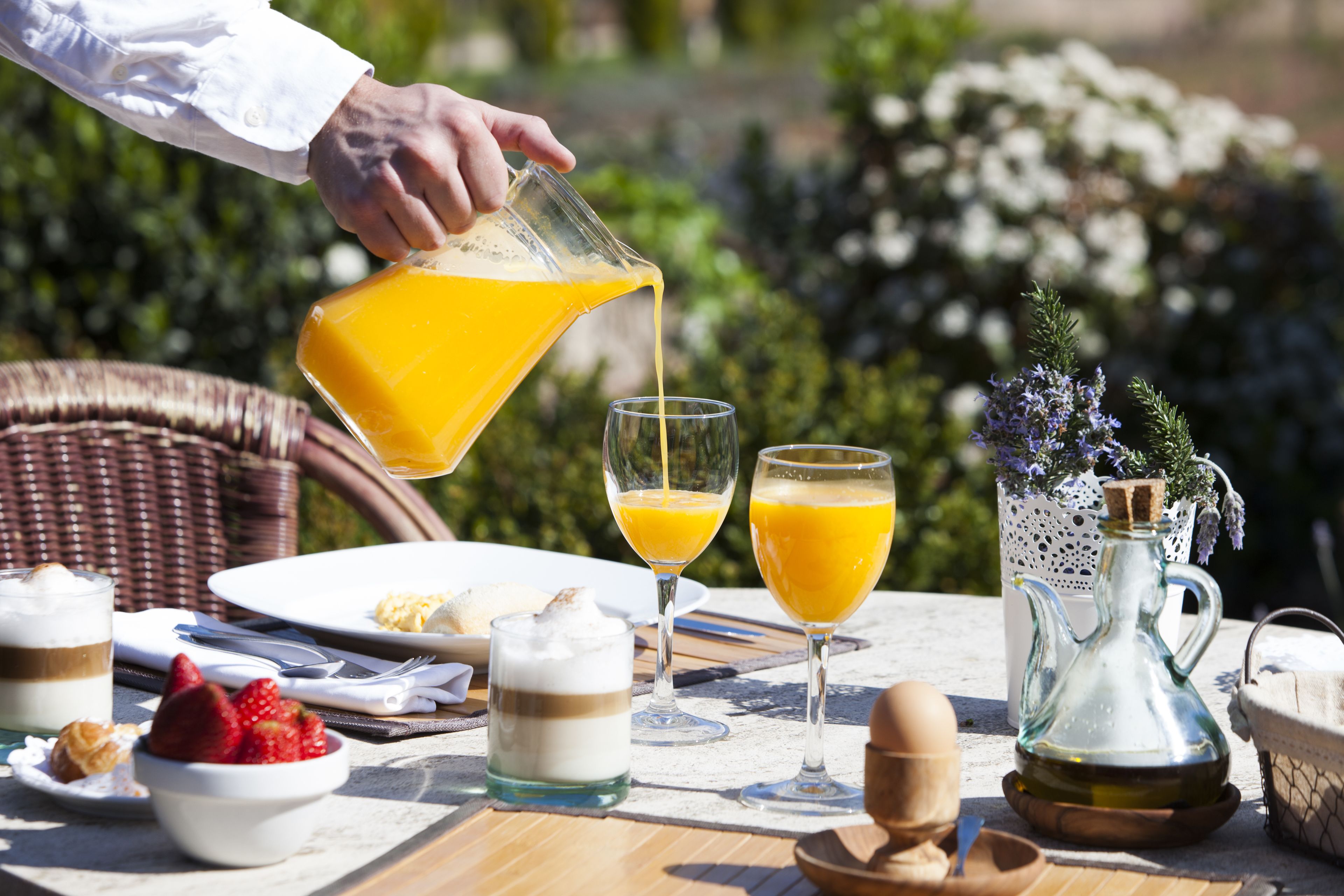A breakfast table with a pitcher of orange juice, two glasses, a bowl of strawberries, a glass of milk, and a pitcher of oil.