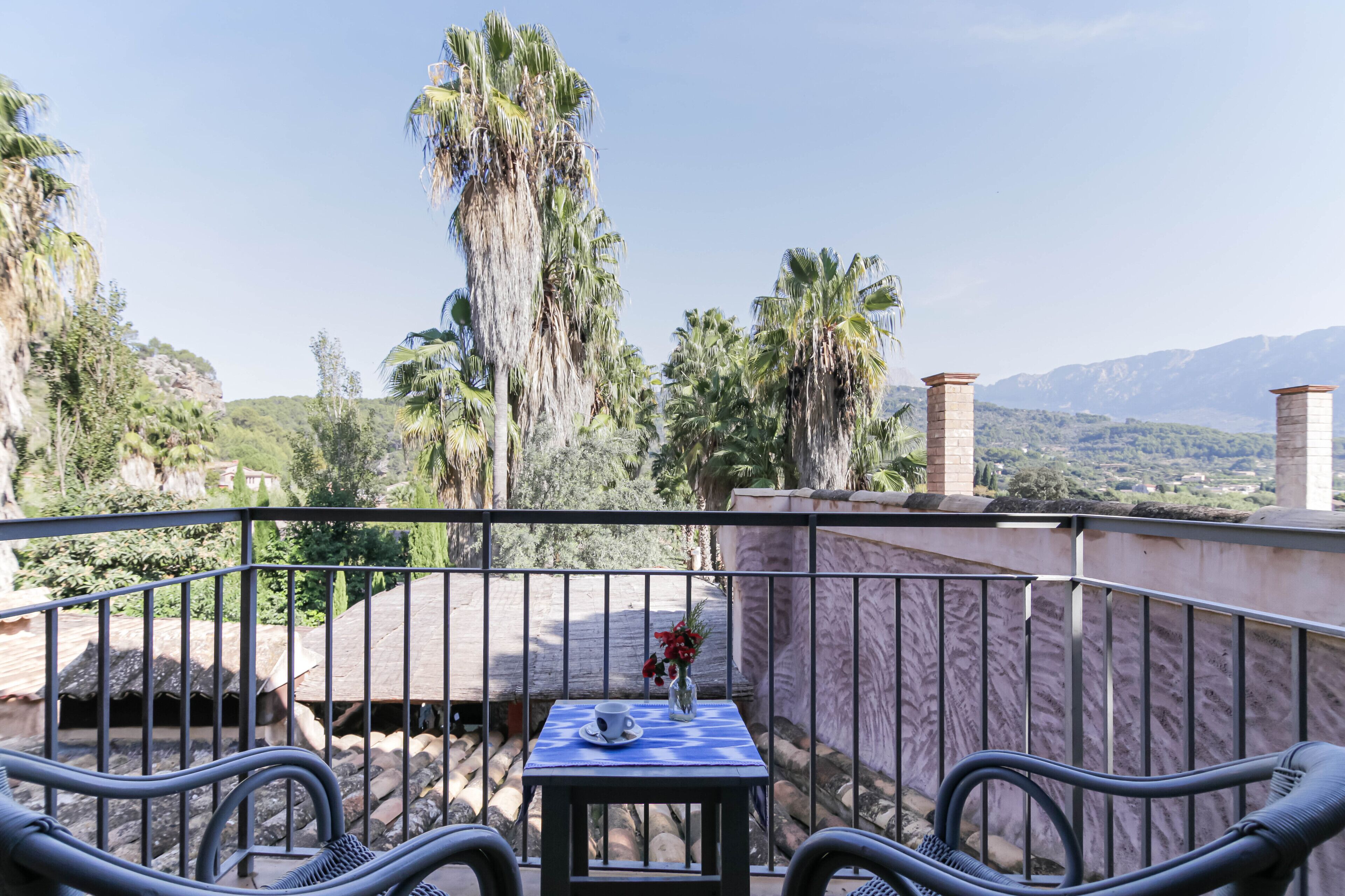 Un balcon avec une table et des chaises, donnant sur un paysage montagneux parsemé de palmiers.
