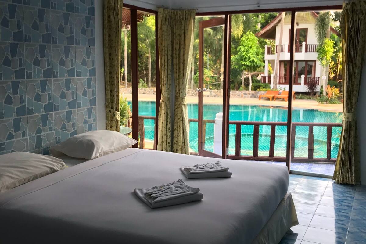 A hotel room with a large bed, a view of a swimming pool, and a balcony.