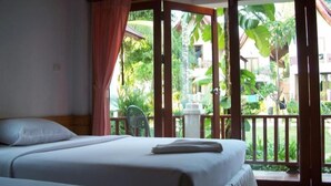 A hotel room with a bed, a view of a garden through a sliding door, and a balcony with a chair. - Koh Chang Thai Garden Hill Resort (Ko Chang)