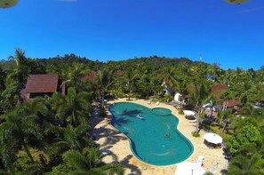Una piscina rodeada de palmeras y sillas de playa, con un edificio al fondo.