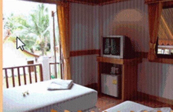 Una habitación con cama, una mesita, televisor y ventana con cortinas.