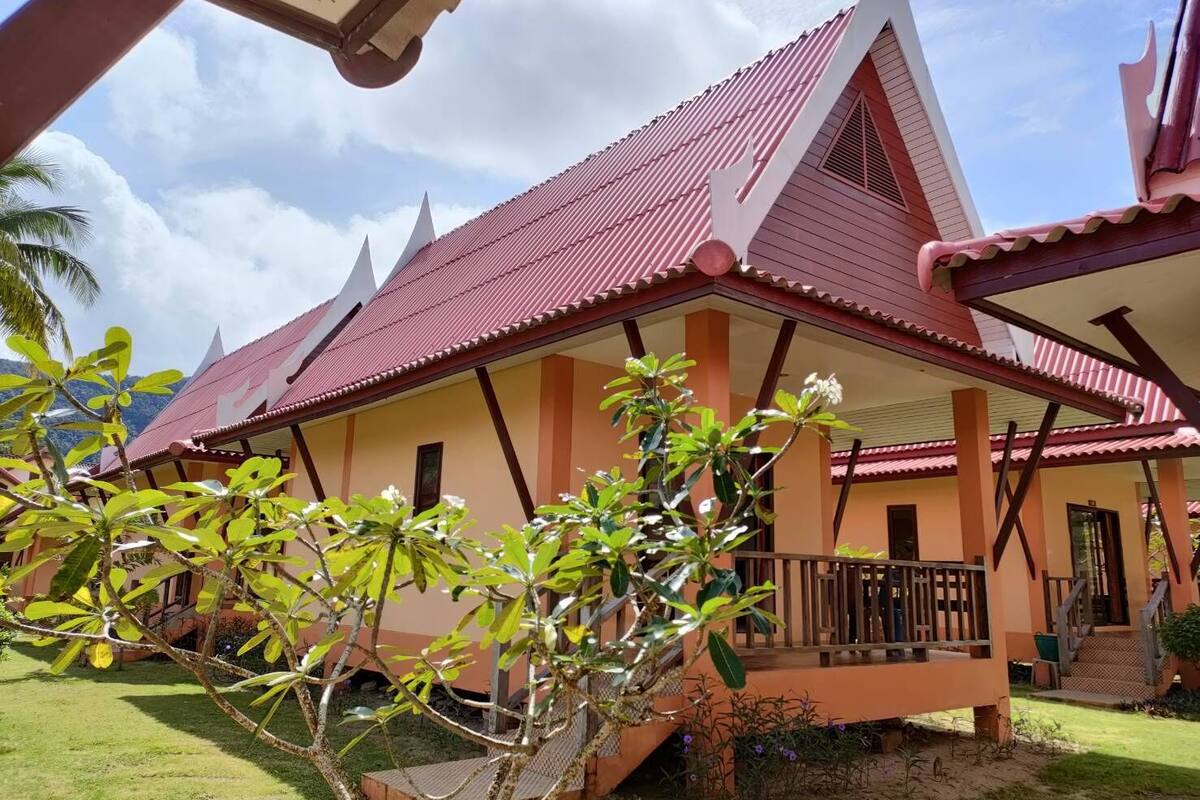Una casa tradicional con techo rojo, un balcón y un jardín con plantas.