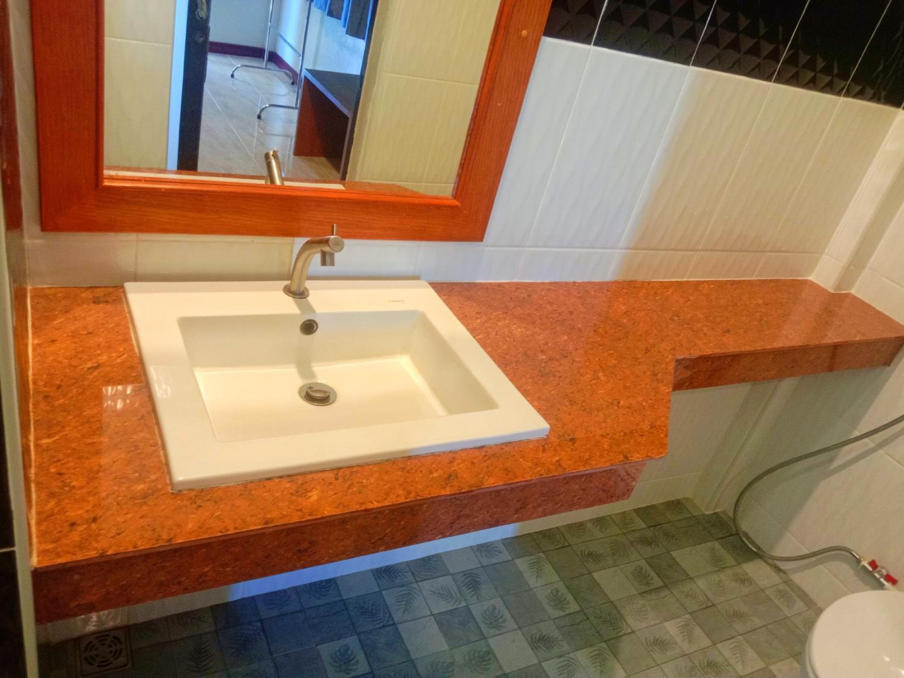 Un baño con un lavamanos blanco, un espejo encima y suelo de baldosas.