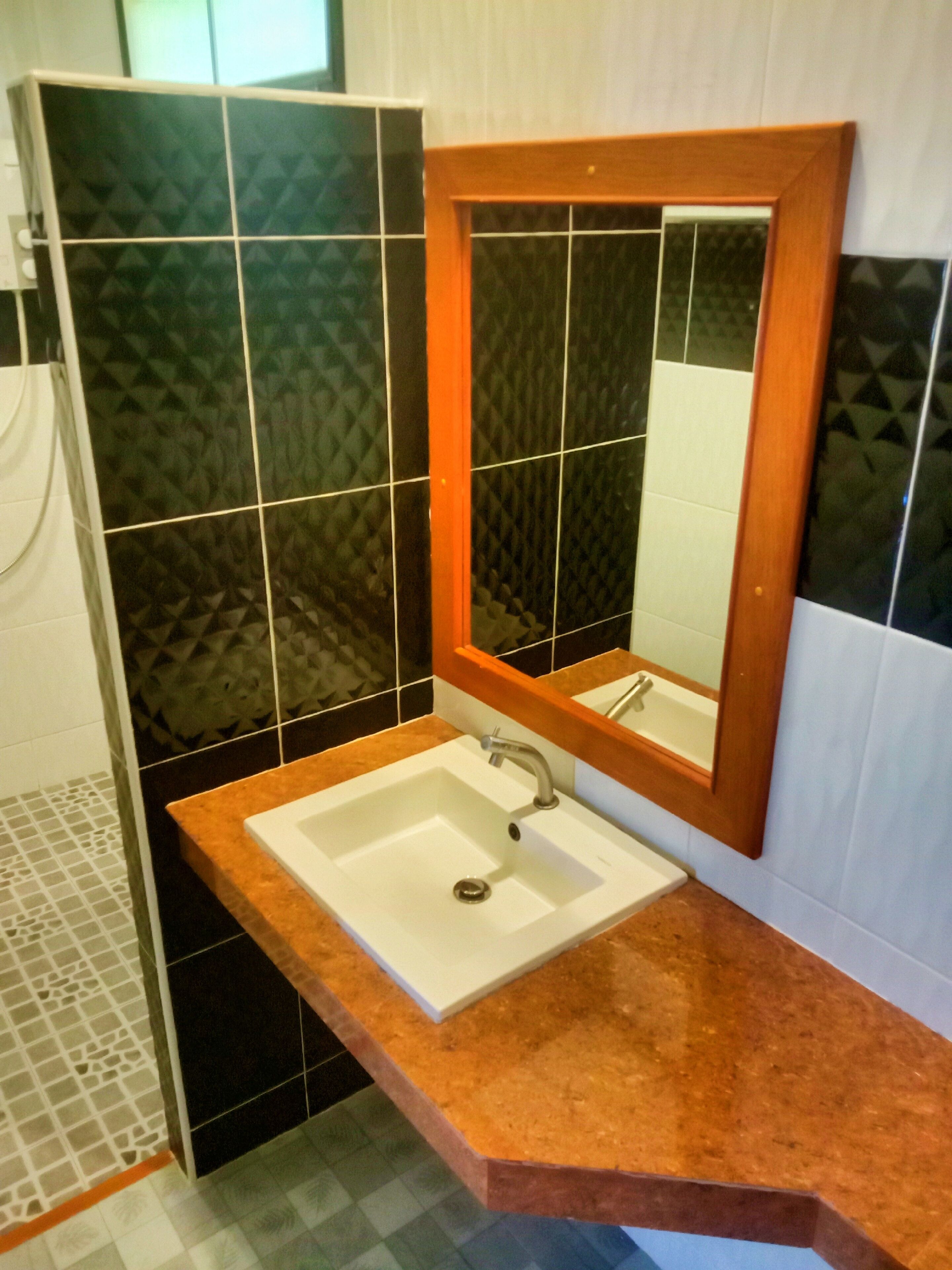 Un bagno con un lavandino bianco, uno specchio e piastrelle nere decorate.