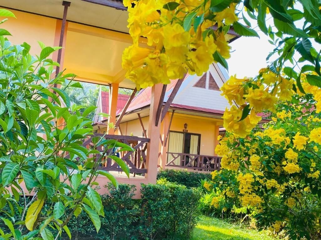 A yellow building with a balcony, surrounded by lush greenery and yellow flowers.
