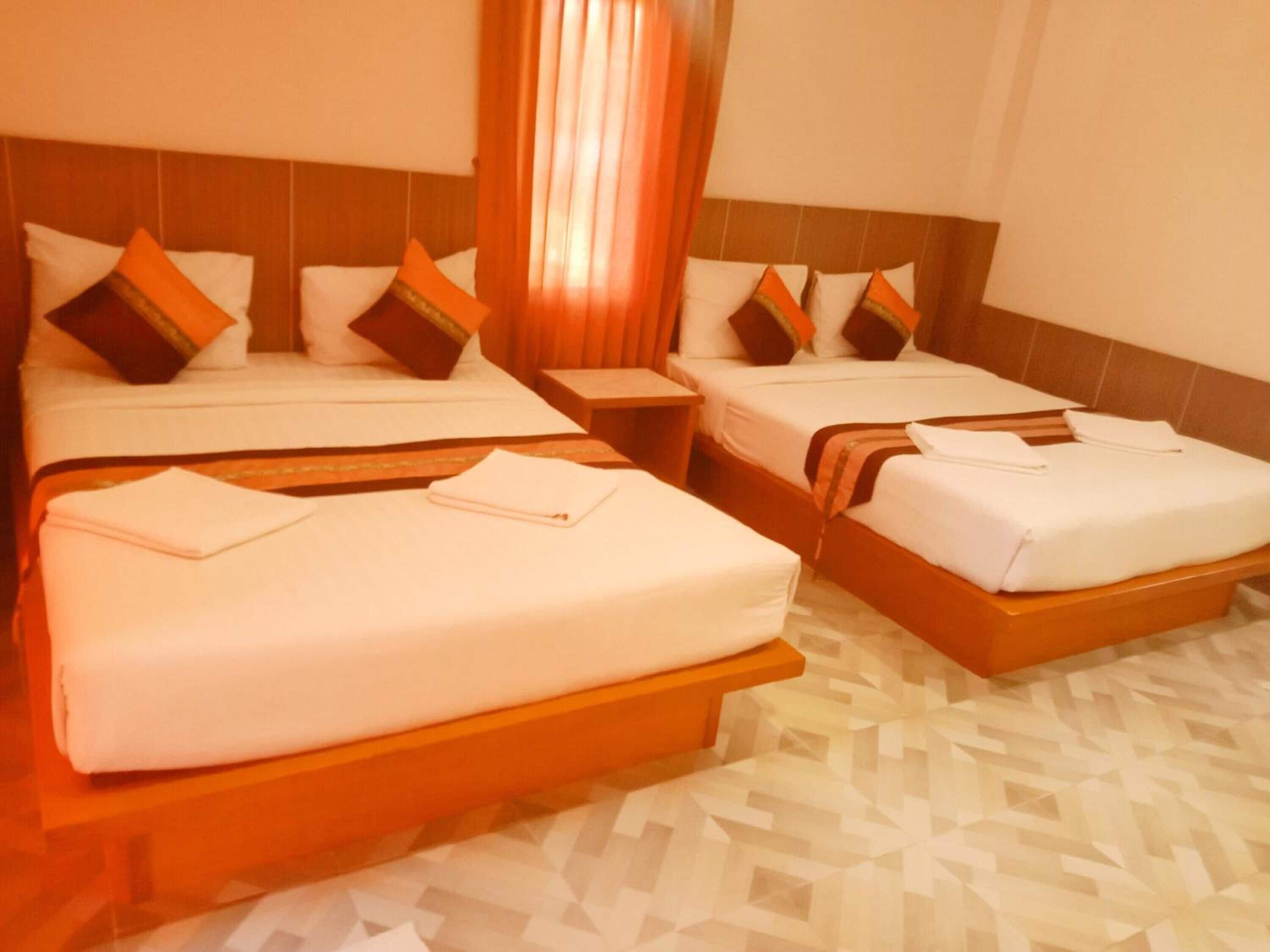 A hotel room with two beds, each with white linens and orange headboards. There are wooden nightstands and a patterned floor.